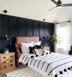 a bedroom with black and white bedding, wooden dressers, and potted plants