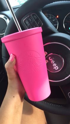 a person holding a pink starbucks cup in their hand next to a car steering wheel