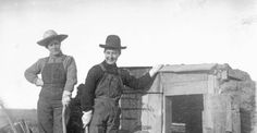 two men standing next to each other in front of a fire place wearing hats and overalls