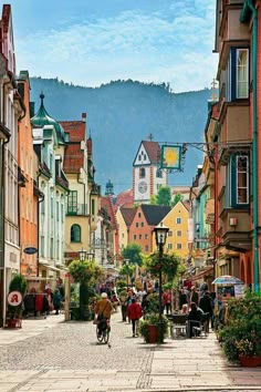 an image of a city street with people walking and sitting on the benches in front of buildings