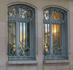 two windows with blue iron bars on the side of each window and one has a clock in it