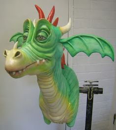 a green and yellow dragon statue sitting on top of a table next to a white brick wall