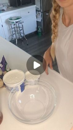 a woman standing in front of a white counter top with food on it and a glass bowl