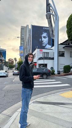 a man standing on the side of a road next to a street sign and buildings