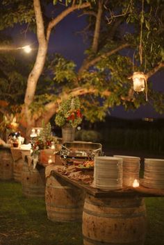 a table with plates and cups on it in front of a large tree at night