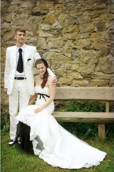 a bride and groom posing for a photo in front of a stone wall with a wooden bench