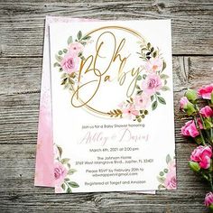 a pink and gold baby shower with flowers on the side, next to it's envelope