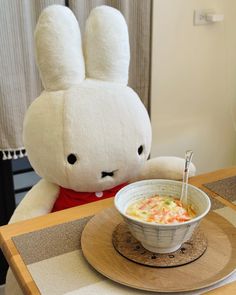 a bowl of soup sits on a table next to a stuffed animal, which looks like a bunny