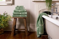 a stack of green towels sitting on top of a wooden stool next to a bath tub