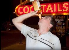 a man drinking from a bottle in front of a neon sign that reads cocktails