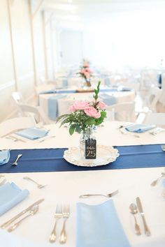 the table is set with blue and white linens, silverware, and pink flowers