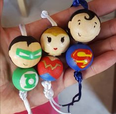 a hand is holding several small wooden toy balls with different designs on them, including superman and wonder woman faces