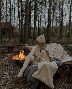 a woman sitting next to a fire in the woods