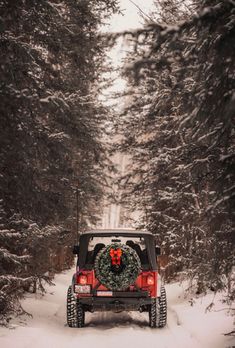 a jeep driving down a snow covered road with a wreath on the back of it