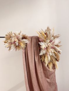 an arrangement of dried flowers on a drape in front of a white wall and curtain