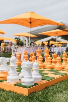 a giant chess set on the grass with an umbrella in the background