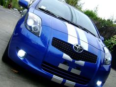 the front end of a blue car with white stripes on it's hood and headlights