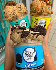 three ice creams with cookie dough and oreo cookies in them are being held by someone