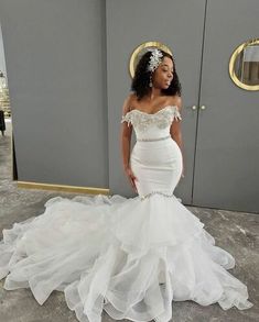 a woman in a white wedding dress standing next to a gray wall wearing a tiara