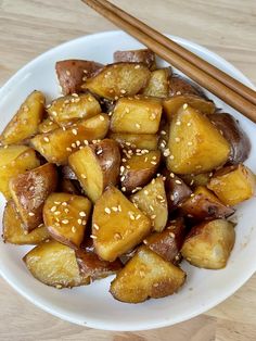 a white plate topped with fried potatoes and chopsticks next to a wooden table