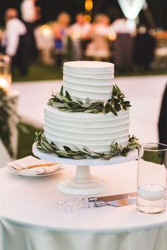 a white wedding cake sitting on top of a table next to a glass of water