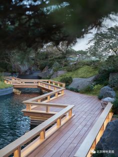 a wooden bridge over a body of water next to rocks and trees with lights on them