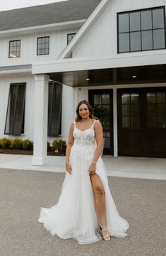 a woman standing in front of a white house wearing a wedding dress and high heels