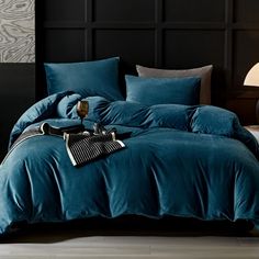 a bed with blue comforters and pillows in a dark colored room, next to a lamp