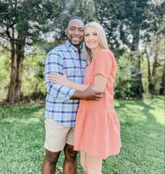 a man and woman standing in the grass with their arms around each other, smiling at the camera