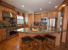 a large kitchen with wooden cabinets and stainless steel appliances, along with two bar stools