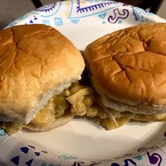 two sandwiches sitting on top of a white plate next to each other in front of a blue and purple flowered paper plate