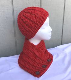 a mannequin head wearing a red knitted hat and scarf with buttons on it