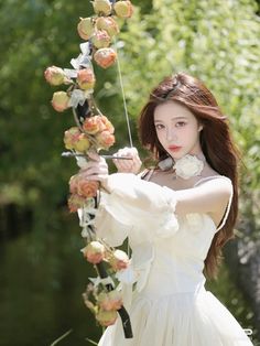 a woman in a white dress is holding flowers on a stick with her hands and looking at the camera