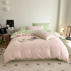 a bed with pink and green comforters in a white room next to a desk