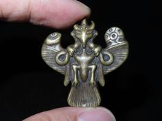 a hand holding a small metal object in it's right hand, with an intricate design on the top