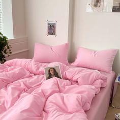 a bed covered in pink sheets and pillows with a magazine laying on top of it