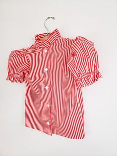 ❤Made to order. Vintage inspired shirt, perfect for any occasion. Red and white striped shirt for girls, featuring a ruffle collar and big puffy sleeves gathered with elastic. Cotton poplin fabric☆☆ Listing is for the shirt only☆☆▪︎Matching pieces here▪︎https://www.etsy.com/shop/CeciliaAndMae?ref=simple-shop-header-name&listing_id=678216147&section_id=26035288•More shirt options here•https://www.etsy.com/shop/CeciliaAndMae?ref=simple-shop-header-name&listing_id=678216147&section_ Preppy Top With Striped Collar For Spring, Spring Shirt With Ruffles And Puff Sleeves, Cute Collared Blouse With Ruffles, Cotton Shirt With Ruffle Sleeves, Cotton Fitted Shirt With Puff Sleeves, Fitted Cotton Shirt With Puff Sleeves, Cute Ruffled Puff Sleeve Tops, White Vertical Stripes Blouse For Spring, Cute Summer Shirt With Ruffles