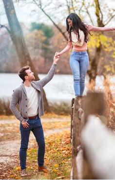 a man holding the hand of a woman on top of a wooden fence in an autumn park