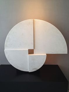 a white sculpture sitting on top of a black table next to a light that is turned on