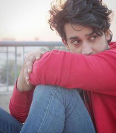 a young man sitting on the ground with his arms crossed and looking at the camera