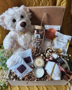 a white teddy bear sitting in a box filled with treats and other things to eat