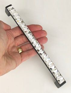 a hand holding a metal object that looks like a bar with diamonds on it's sides