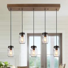 four mason jar lights hanging from a wooden beam in a kitchen with white walls and windows