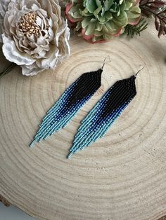 two blue and black seed beaded earrings sitting on top of a piece of wood