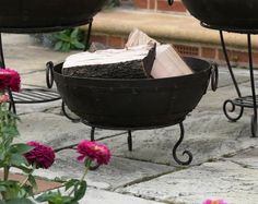 two black iron planters sitting on top of a stone floor next to flowers and potted plants