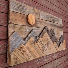 a wooden wall hanging on the side of a red building with mountains painted on it