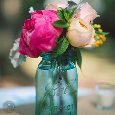 pink and white flowers in a blue mason jar on a table with two glass glasses