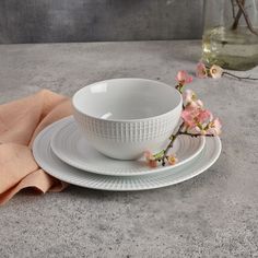 a white bowl and saucer sitting on top of a plate next to a pink napkin