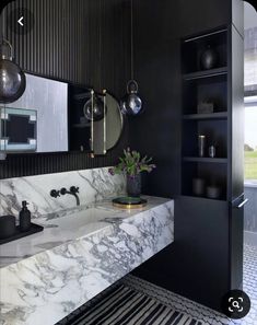 a black and white bathroom with marble counter tops, gold accents and hanging lights above the sink