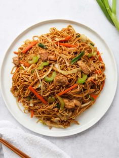 a white plate topped with chicken lo mein next to chopsticks and a napkin